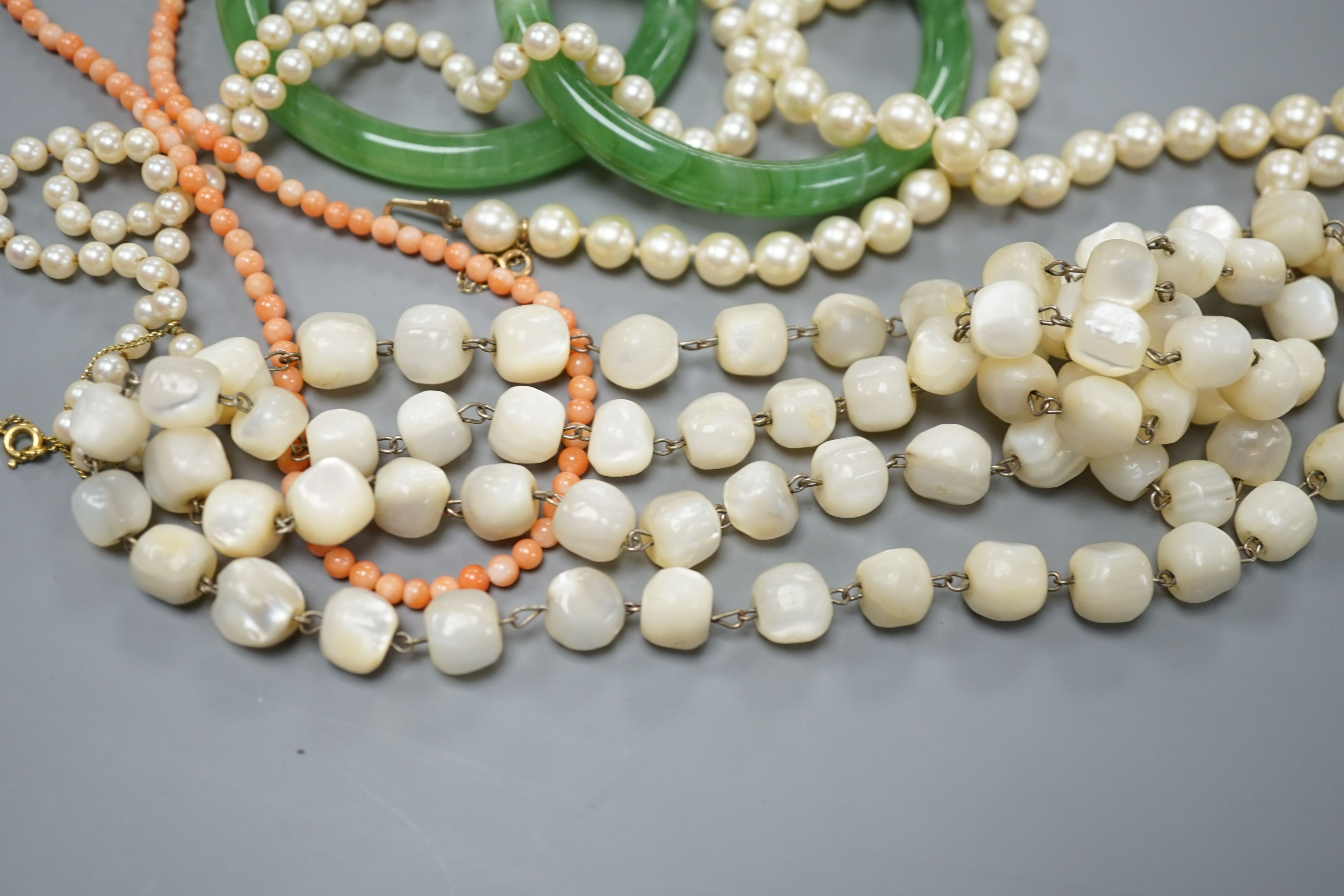 Two single strand cultured pearl necklaces, one with 9ct gold clasp, two green glass bangles, a coral bead necklace and a mother of pearl bead necklace.